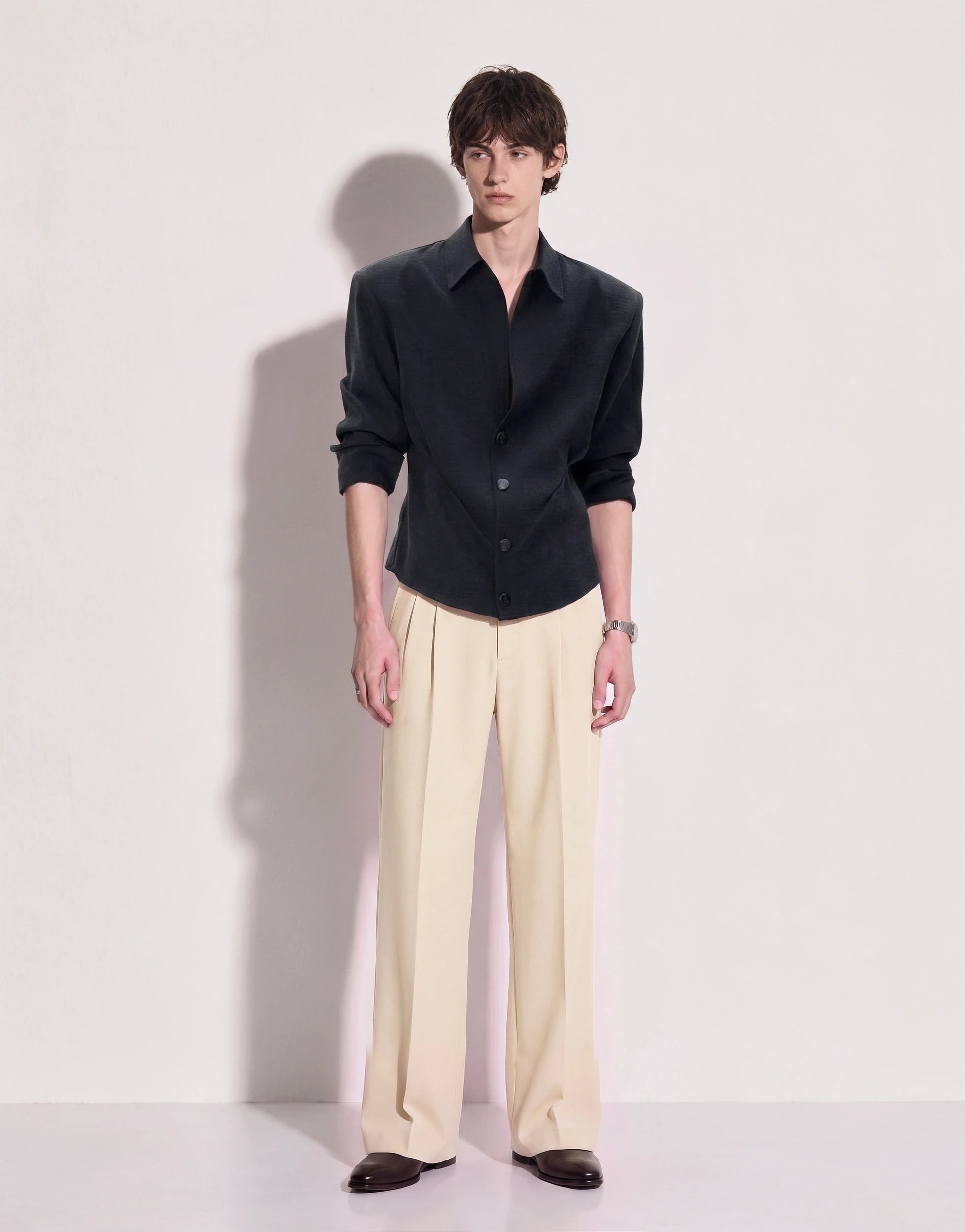 Structured button-up shirt with cinch side detail in dark charcoal, full body front view with cream pleated trousers