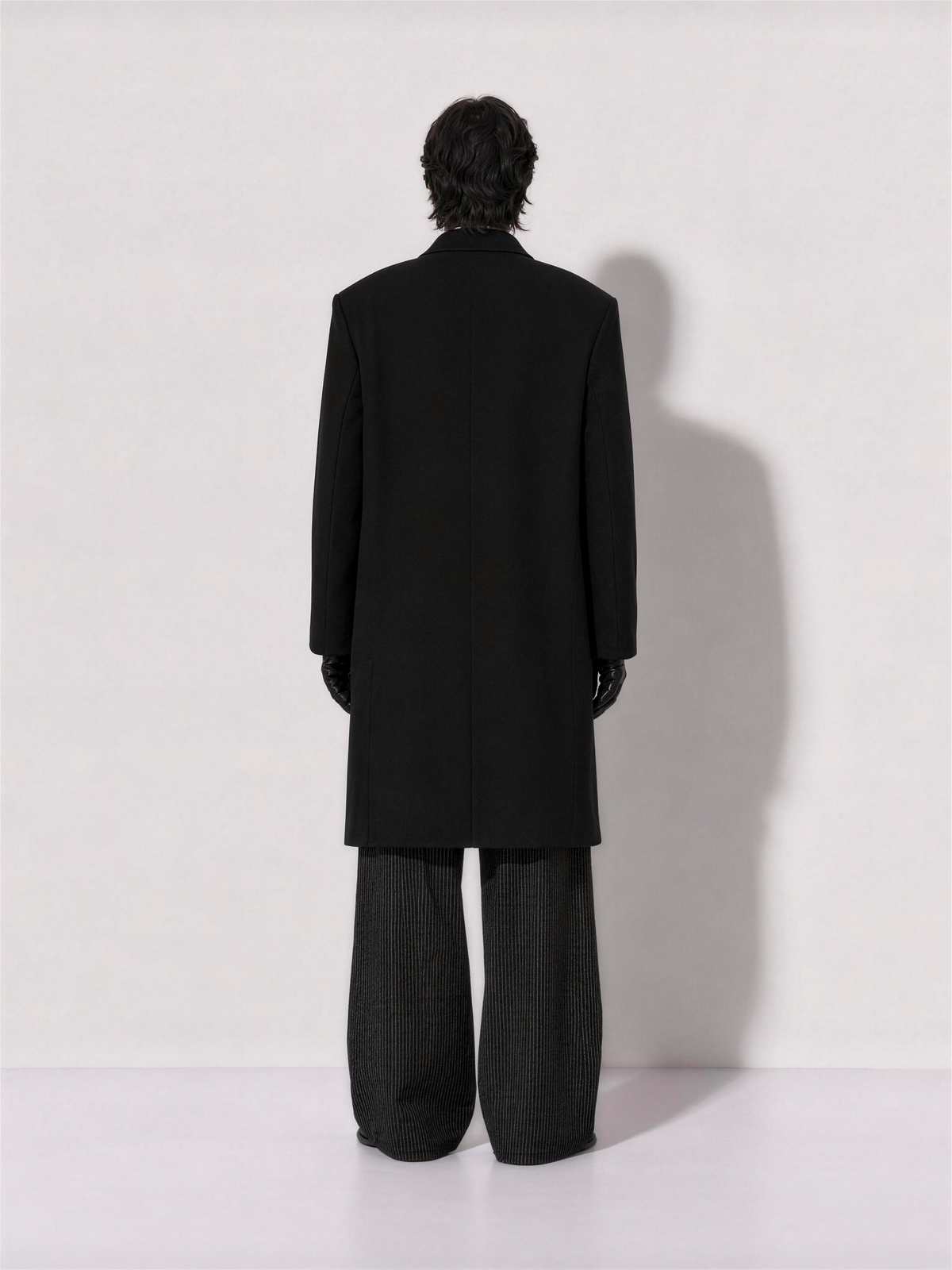 Rear view of the oversized black overcoat showing the dropped shoulder and straight back