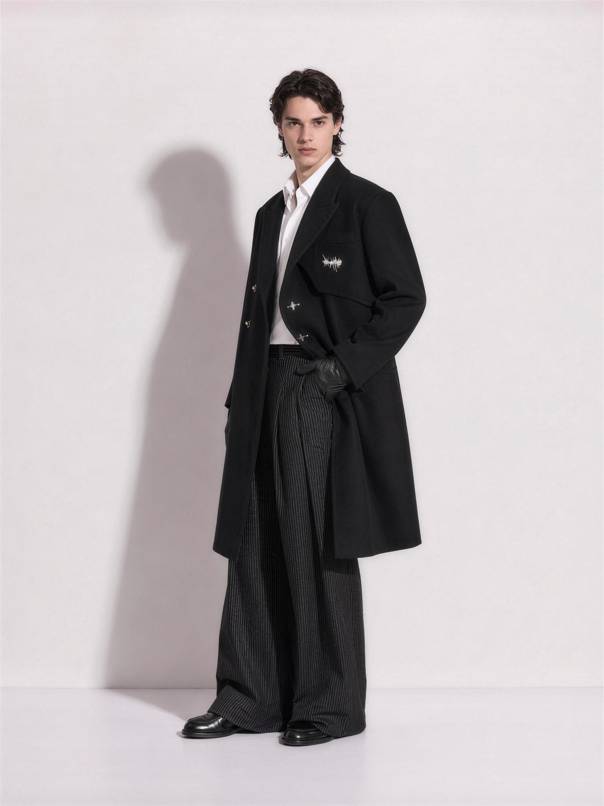 Three-quarter view of the oversized black overcoat showing the asymmetric front panel and silver fireman clasps