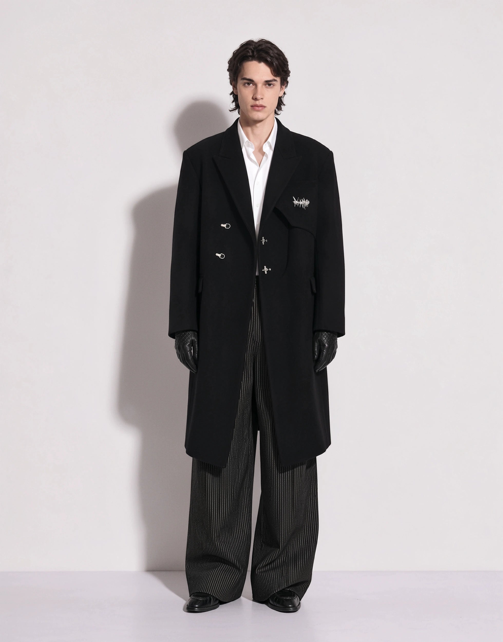 Model wearing the Oversized Asymmetric Overcoat with Fireman Buckle, front view, coat open over a white shirt and pinstripe wide-leg trousers